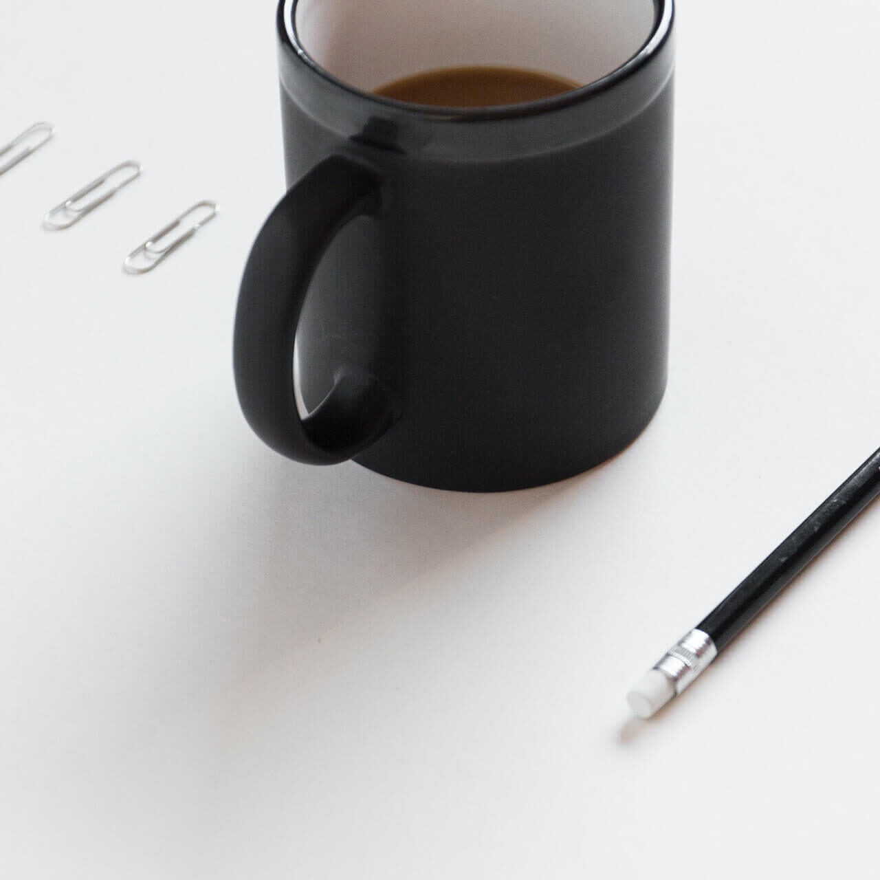 paperclips, coffee mug, pencil, and eraser set up in a line